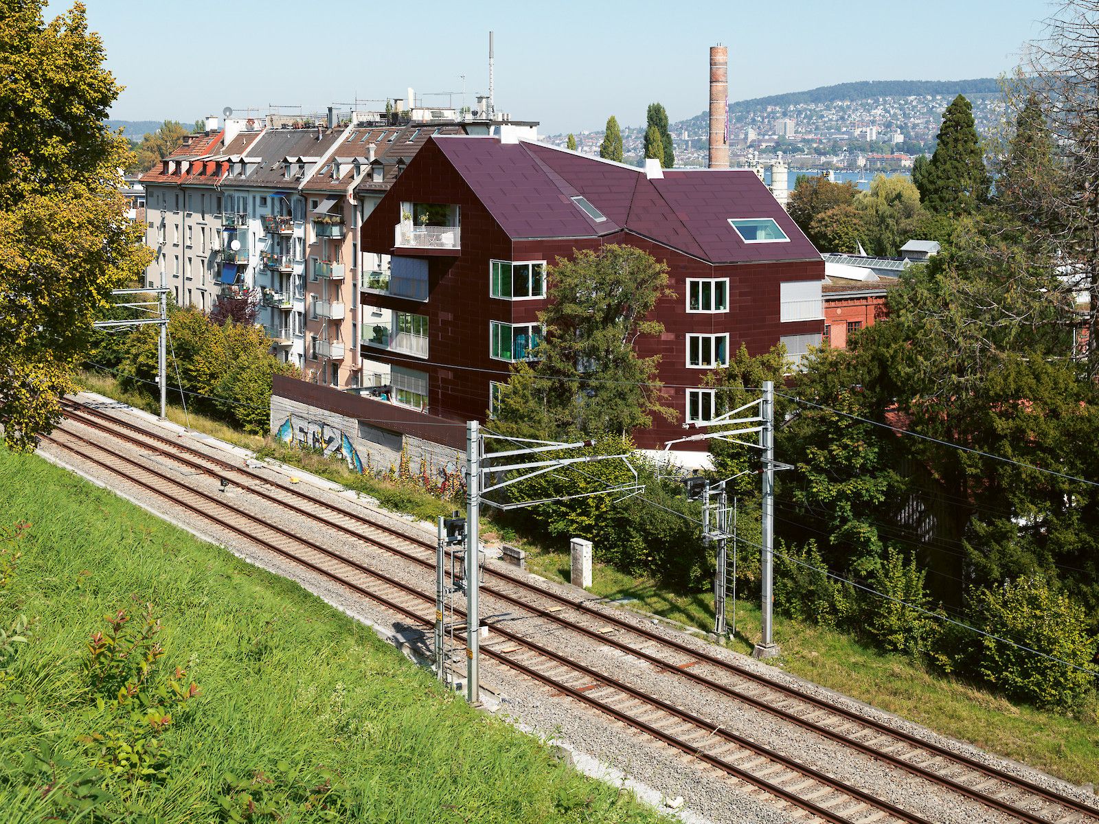 Das Bild zeigt ein von oben aufgenommenes Foto des Wohnhauses Solaris in Zürich, bei dem alle Dach- und Fassadenflächen mit sehr unterschiedlichen Ausrichtungen aus roten PV-Modulen bestehen.