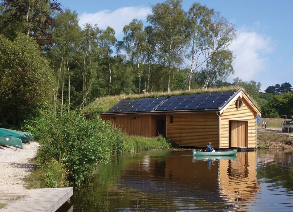Das Foto zeigt ein Bootshaus mit einem aufgeteilten Satteldach: Eine Seite begrünt, die andere Seite mit Photovoltaikmodulen belegt. 